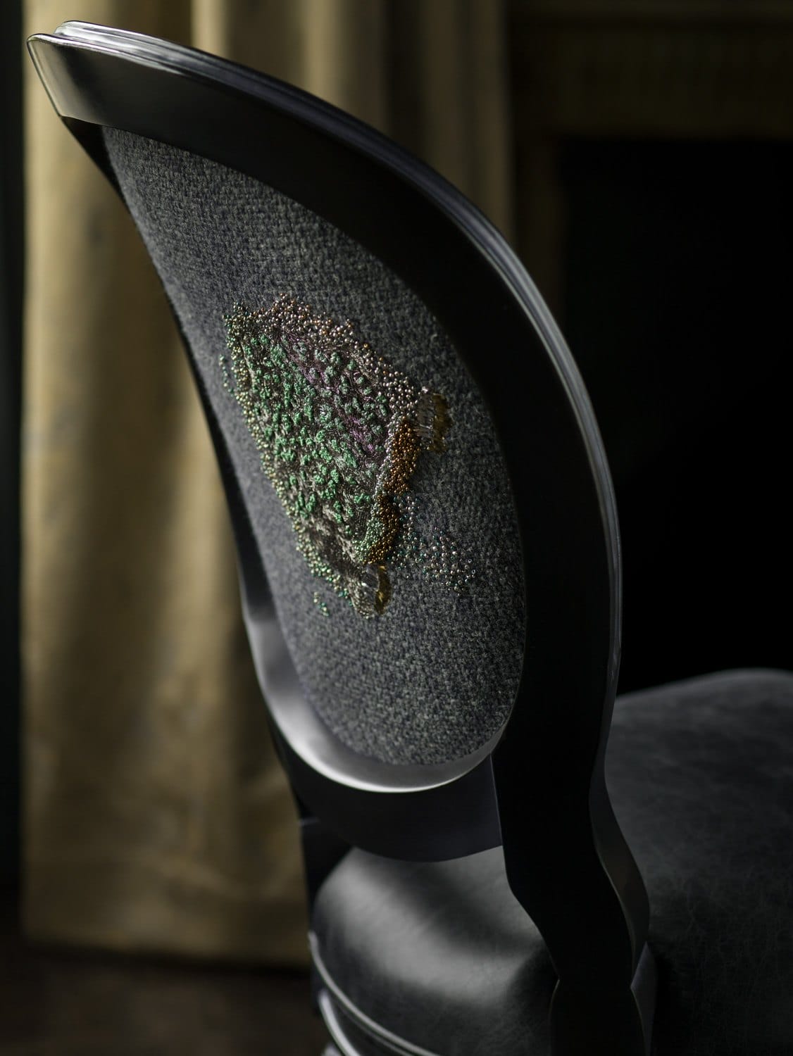 Elegant dark wooden chair with textured fabric and green embroidery on the backrest, set against a dimly lit background.