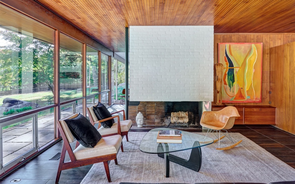 Mid-century modern living room with large windows, white brick fireplace, abstract painting, and stylish furniture.