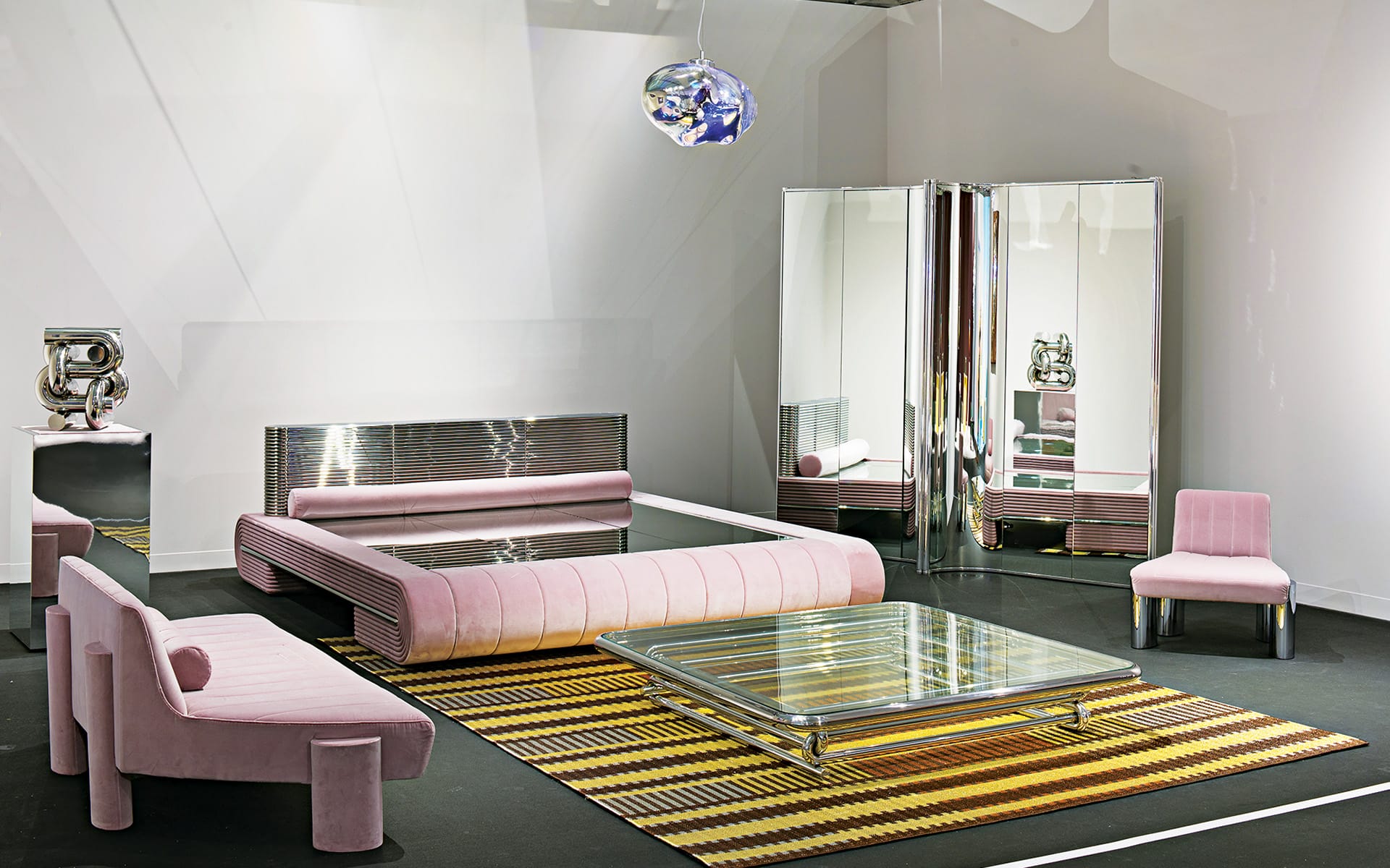Modern room with pink velvet furniture, reflective surfaces, striped rug, and unique lighting fixture.