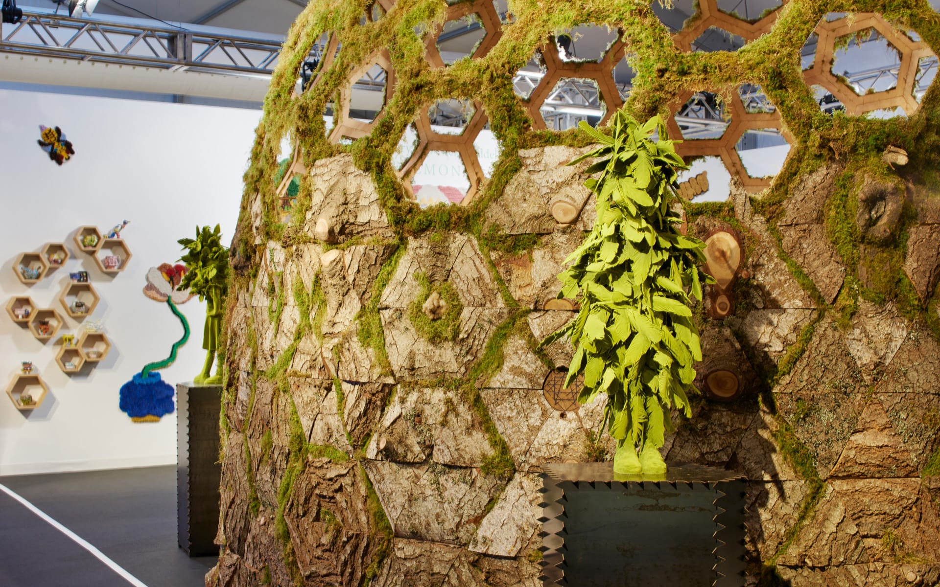 Dome structure covered in hexagonal wooden panels with moss and plants, displayed in an art exhibition space.