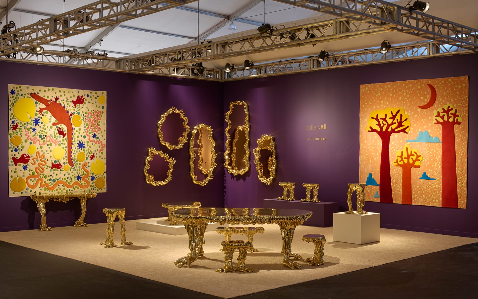 Art exhibition featuring vibrant paintings and gold-toned sculptures in a well-lit gallery with purple walls.