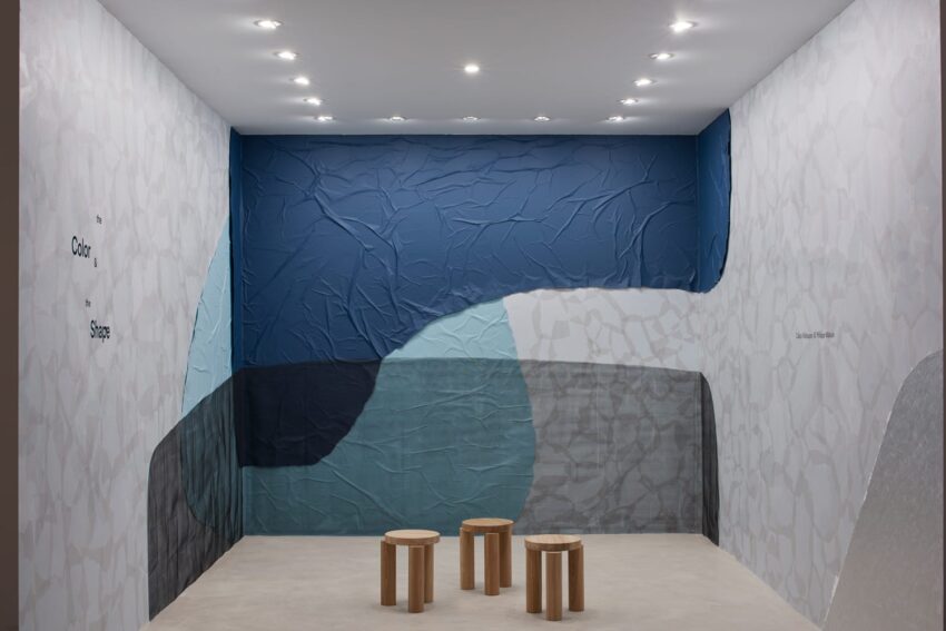 Modern art installation with textured blue and gray walls, spotlights, and three wooden stools in a gallery space.