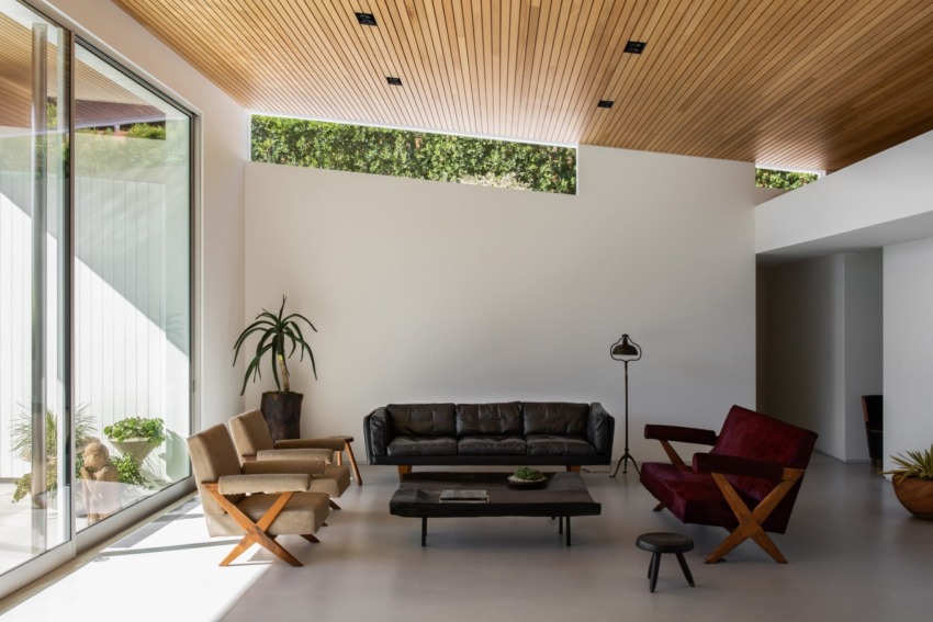 Modern living room with wooden ceiling, large windows, and stylish furniture including a leather couch and armchairs.