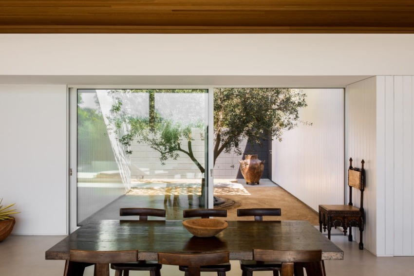 Dining table in modern room with large sliding glass door revealing a small courtyard garden and natural wooden ceiling.