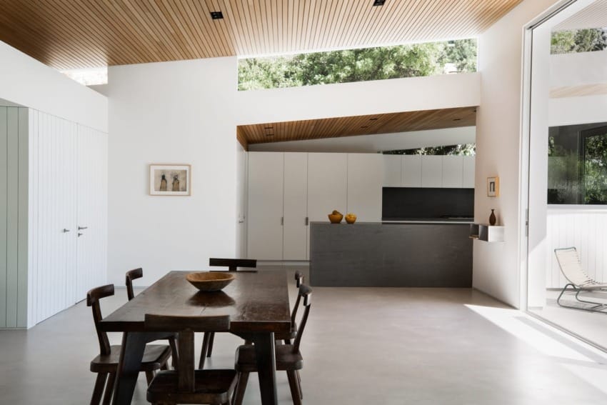 Modern open-plan kitchen and dining area with wooden ceiling, sleek furniture, and large windows showcasing natural light.