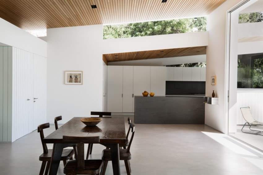 Modern open-plan kitchen and dining area with wooden ceiling, sleek furniture, and large windows showcasing natural light.