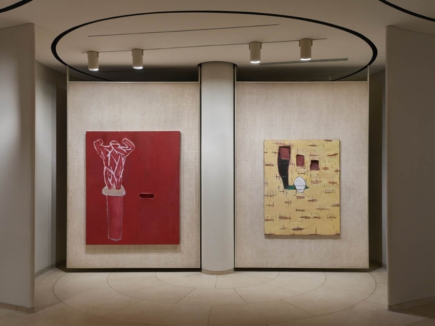 Art gallery hallway with two abstract paintings on display, featuring red and yellow color themes on a curved wall.
