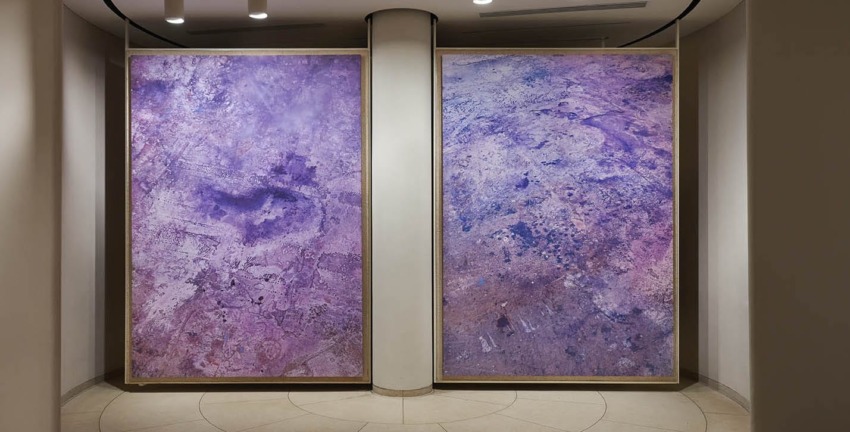 Two large abstract paintings with shades of purple and textures displayed side by side in a well-lit gallery space.