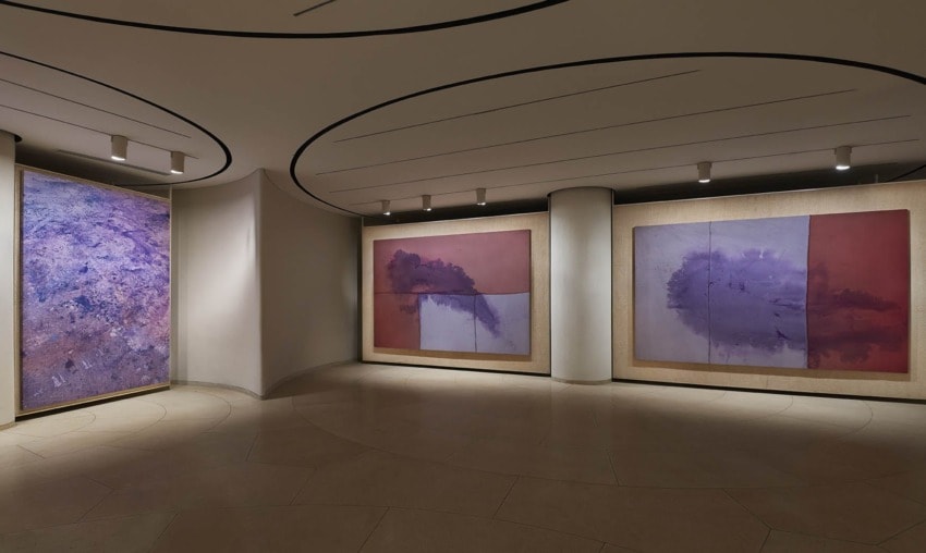 Art gallery interior with curved walls displaying abstract paintings in purple and pink tones, ambient lighting.