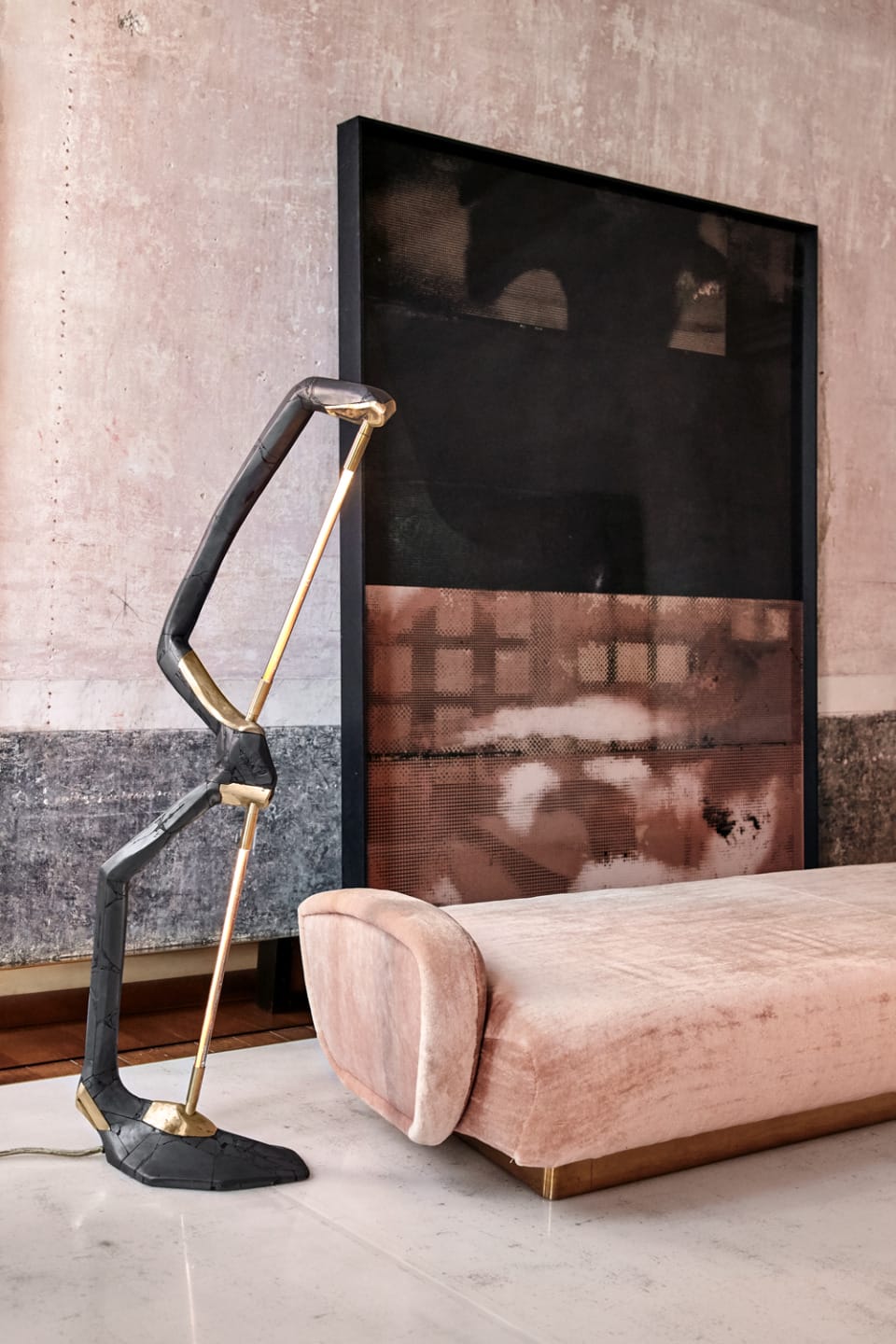 Modern lounge area with a unique floor lamp, abstract wall art, and a plush velvet chaise lounge on a polished floor.