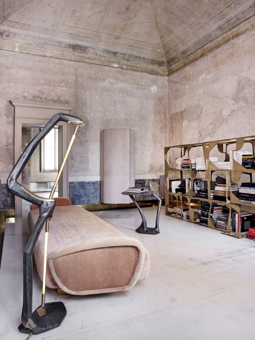 Modern lounge with sculptural lighting, plush sofa, contemporary bookshelves, and rustic walls in a stylish, minimalist room.