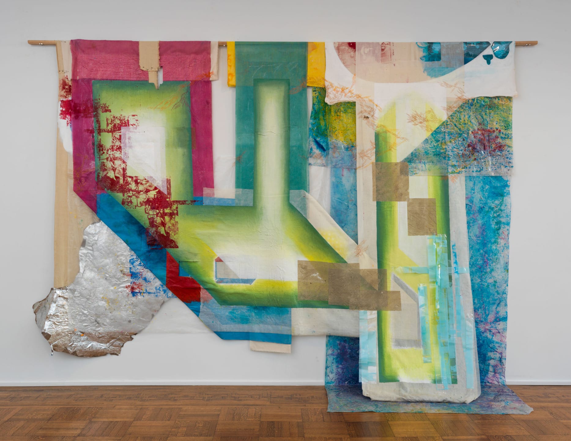 Colorful abstract textile art with layered fabrics and geometric shapes hung against a white wall.