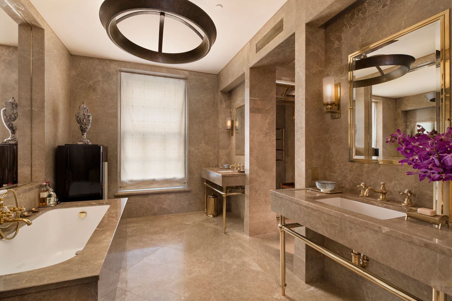 Luxurious marble bathroom with a bathtub, modern fixtures, a large mirror, and a vase with purple flowers.