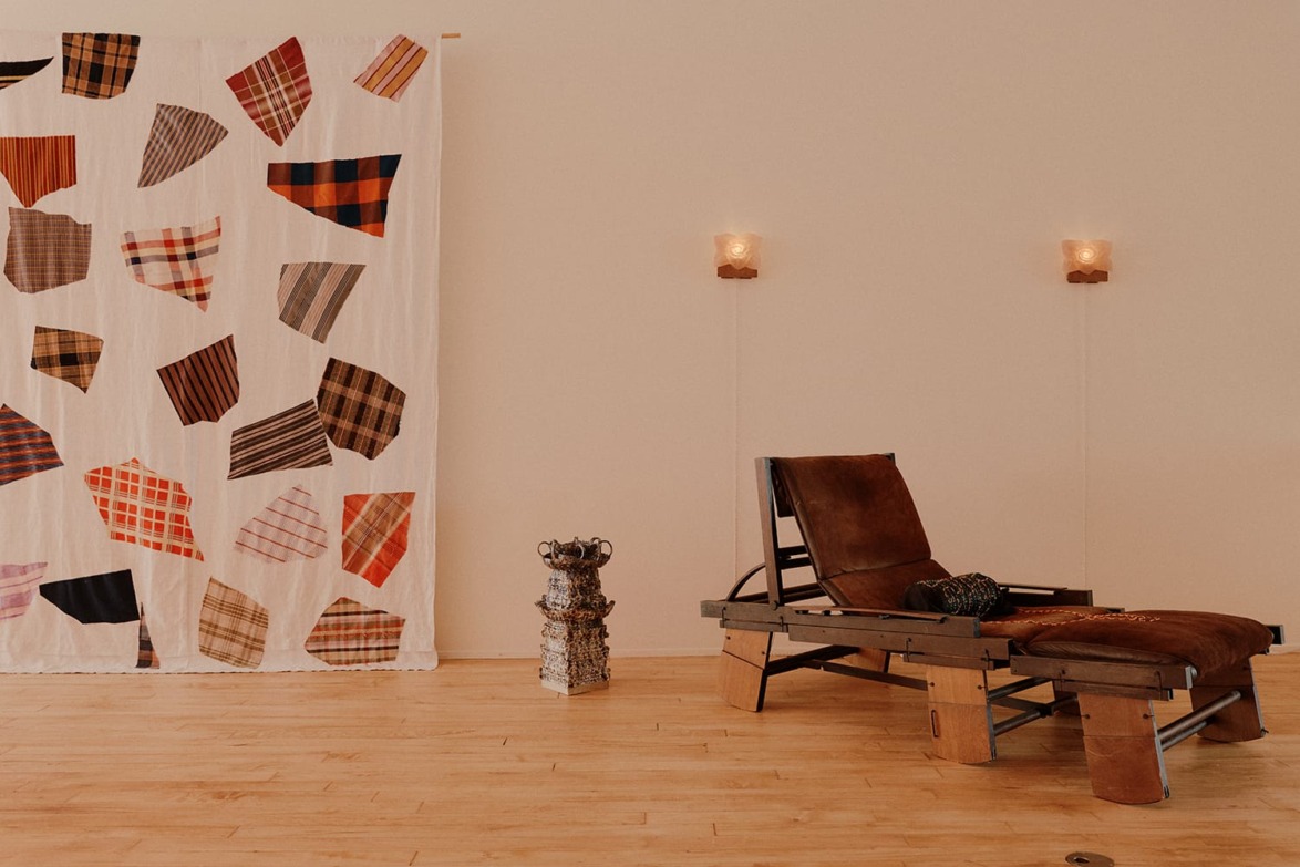 Cozy lounge chair next to a patchwork curtain on a wooden floor with soft lighting.
