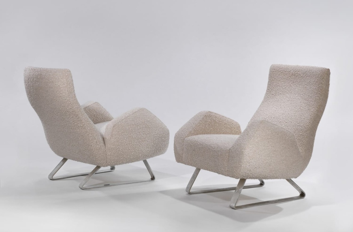 Two modern beige armchairs with sleek metal legs facing each other on a light grey background.