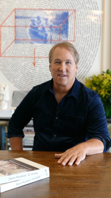 A person sitting at a table with books and a detailed artwork in the background.