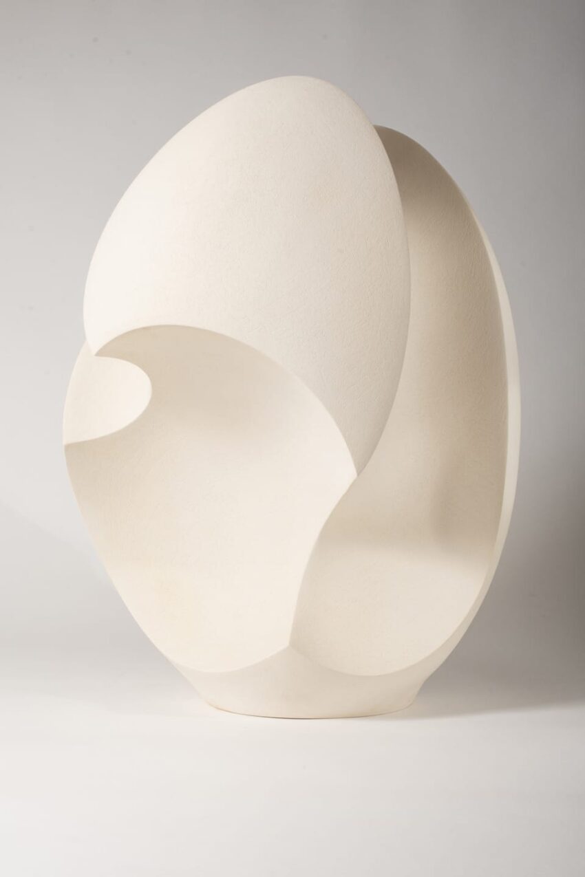 Abstract white sculpture with smooth curves and hollow sections displayed against a neutral background.