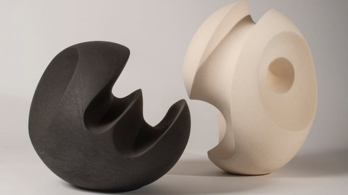 Abstract black and white ceramic sculptures with smooth, curving surfaces on a neutral background.