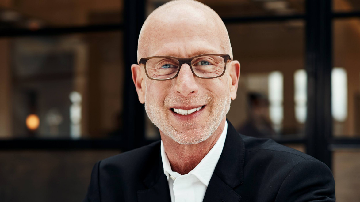 Smiling man wearing glasses and a suit jacket in an office setting.