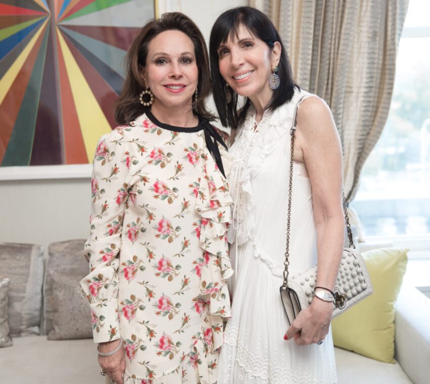 Two women smiling and posing together in a room with colorful abstract artwork in the background.