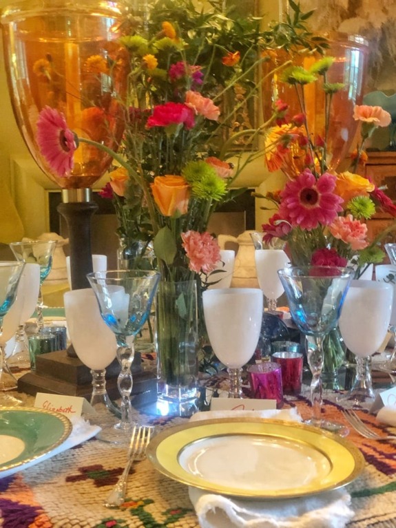 Elegant table setting with colorful flowers, crystal glasses, and decorative plates creating a vibrant and inviting atmosphere.
