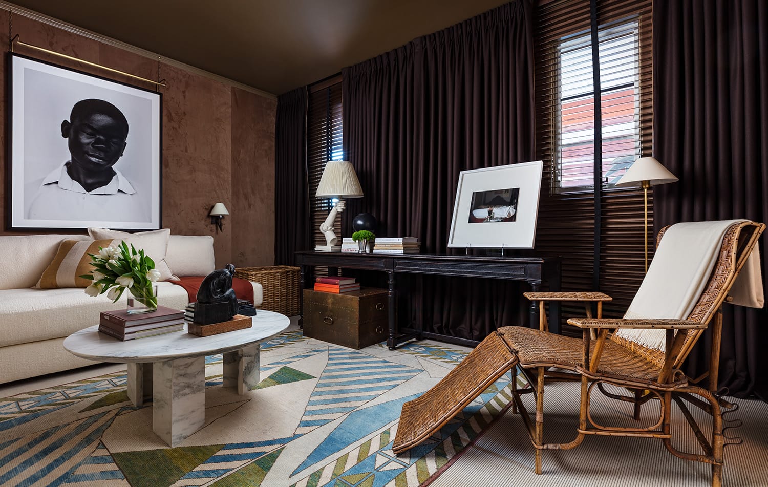 Elegant living room with wicker chair, marble coffee table, framed artwork, and dark curtains. Cozy, stylish interior design.