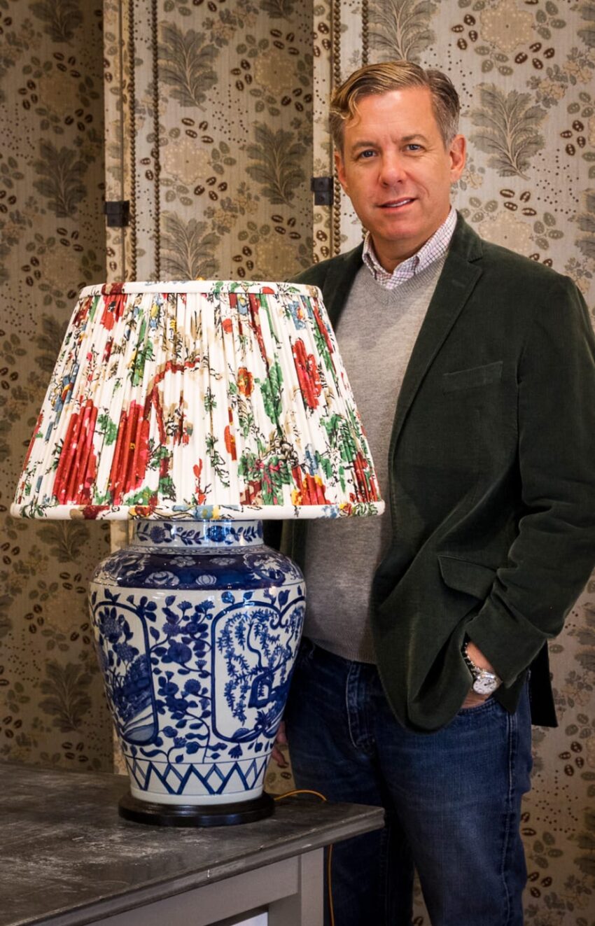 Man in green jacket standing next to a blue and white lamp with a colorful patterned lampshade.