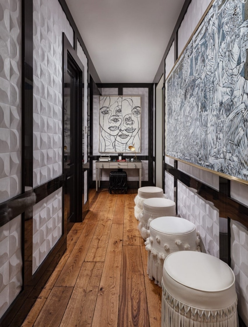 Stylish hallway with textured walls, wooden floor, white stools, and abstract art on walls.