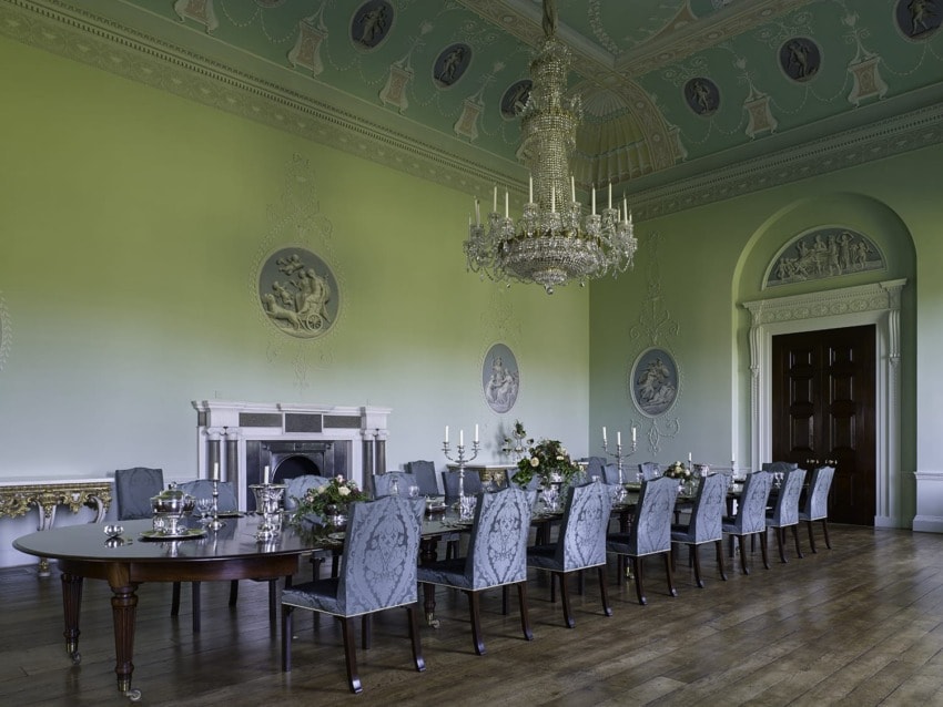 Elegant dining room with long table, ornate chandelier, high ceiling, decorative moldings, and classical wall art.