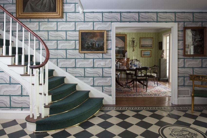 Elegant interior with a staircase, checkered floor, art on walls, and a view into a dining room featuring a patterned rug.