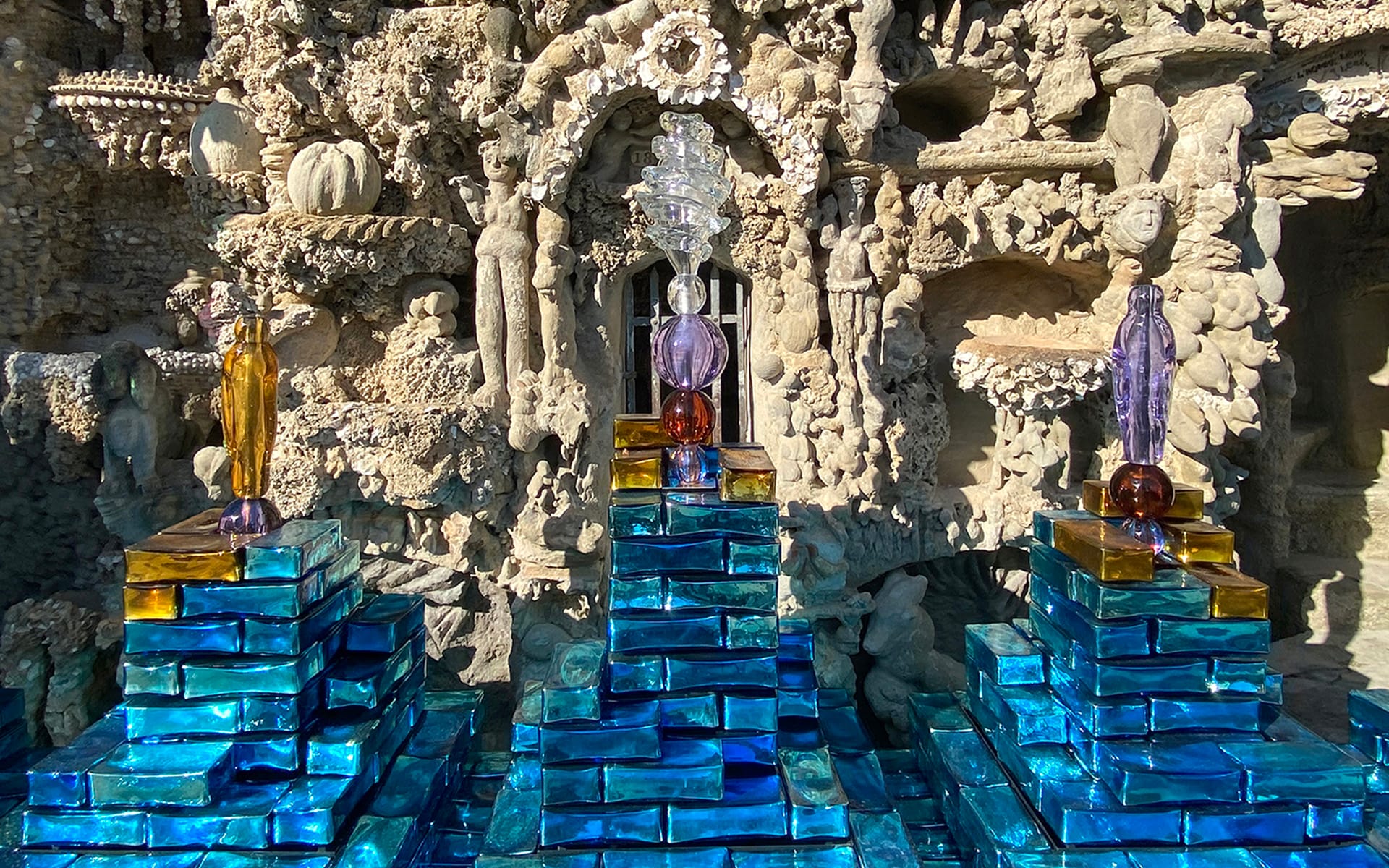 Sculptures and colorful glass structures displayed in front of an intricate stone façade with carved figures and patterns.