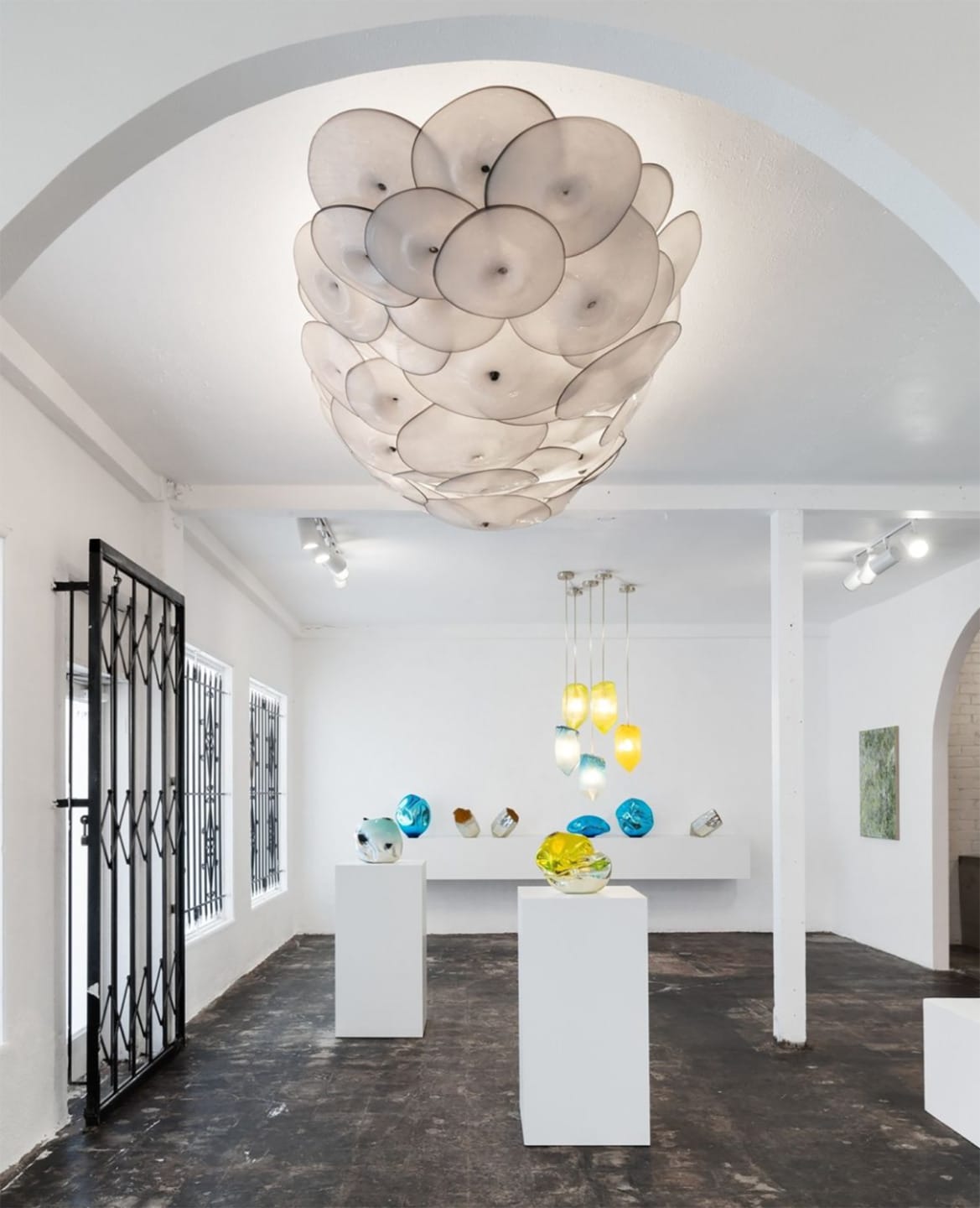 Art gallery interior with glass sculptures on pedestals and a unique circular ceiling installation, white walls and arches.
