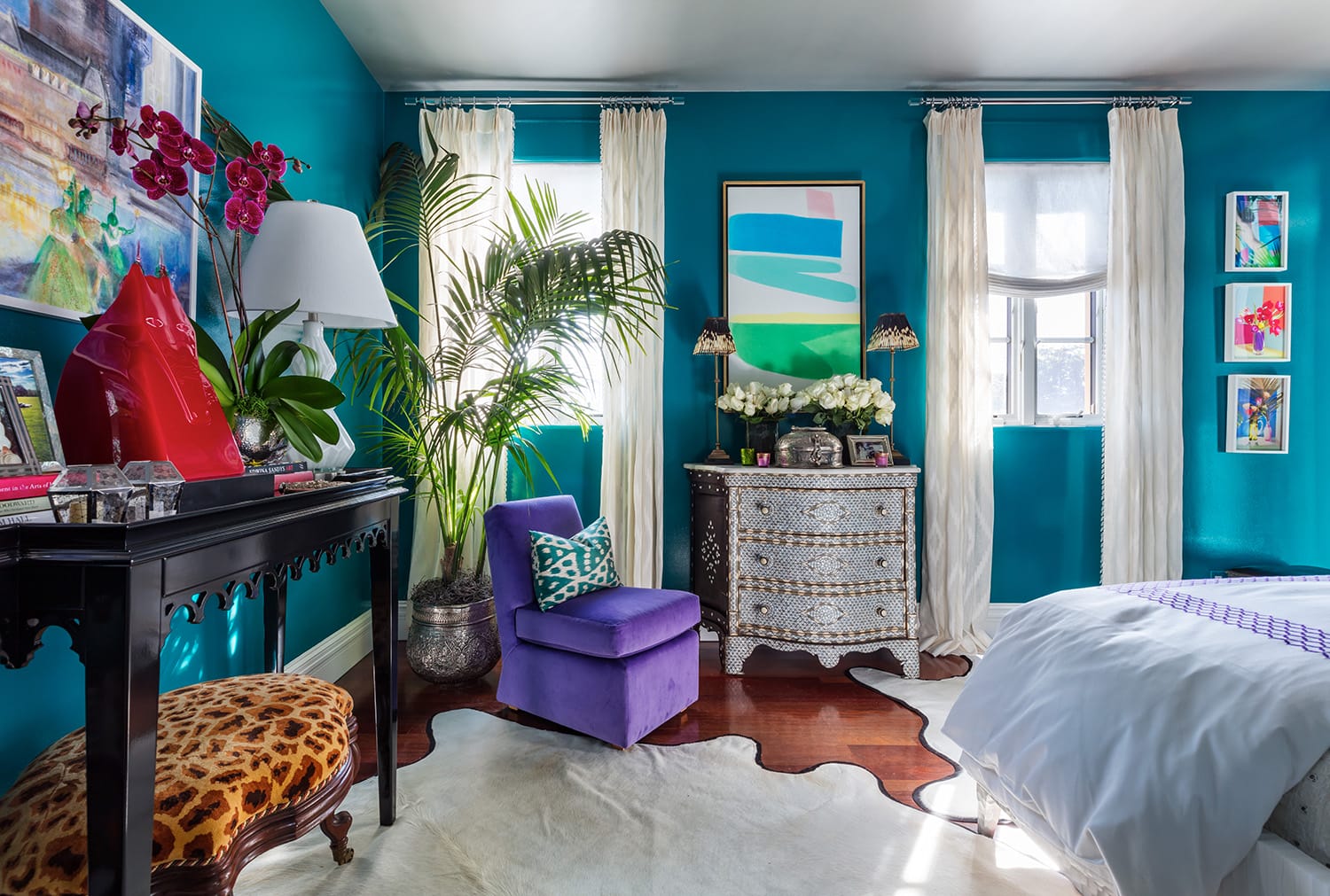Vibrant bedroom with turquoise walls, colorful art, exotic plants, purple chair, and patterned furniture.