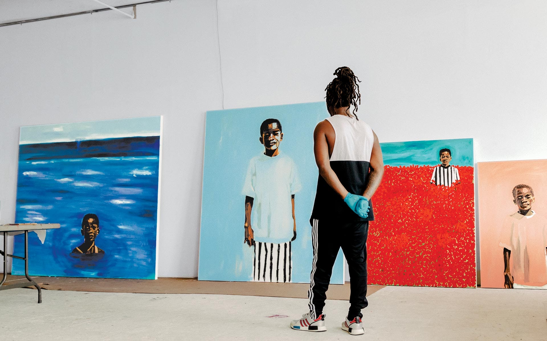 Artist observing colorful portrait paintings on large canvases in a studio setting.