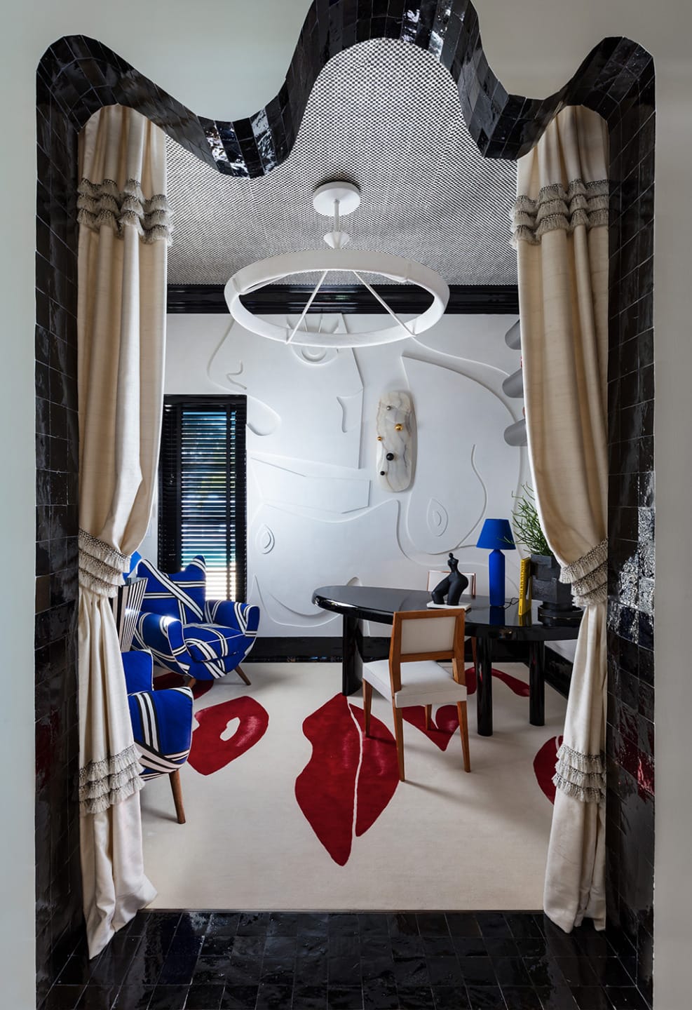 Artistic room with modern decor, blue armchair, abstract rug, and circular chandelier, framed by elegant drapes and black tiles.