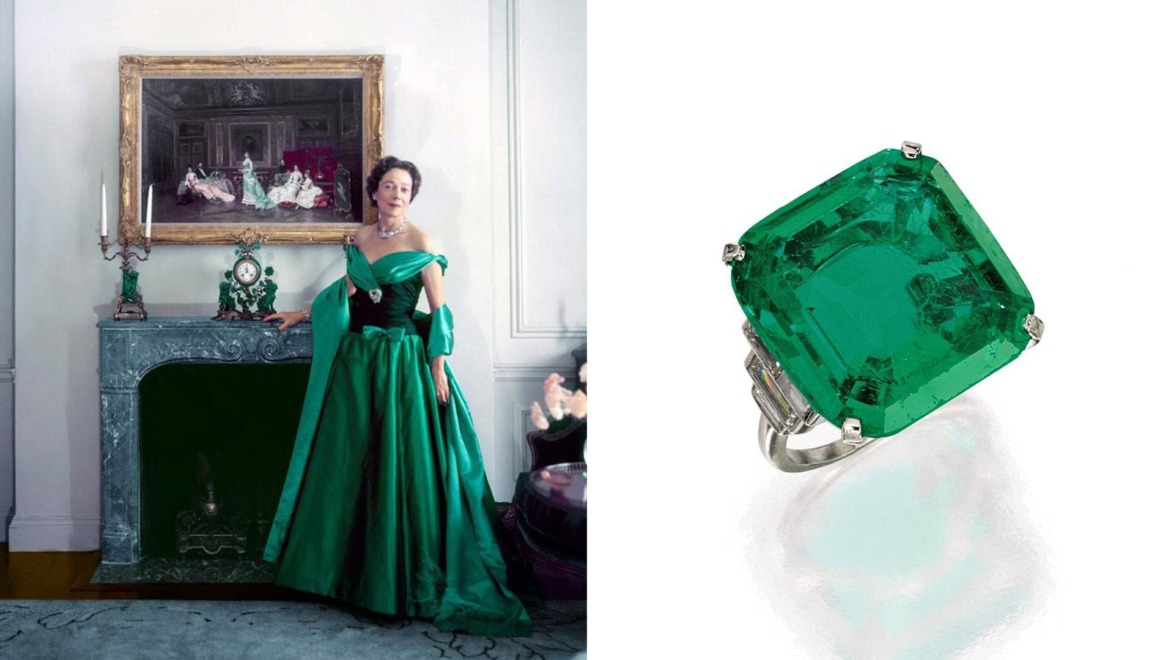 Woman in green gown by fireplace; large emerald ring on white background.