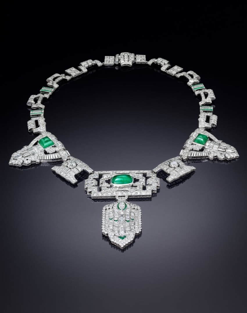 Art Deco necklace with emerald and diamond detailing displayed on a dark background.