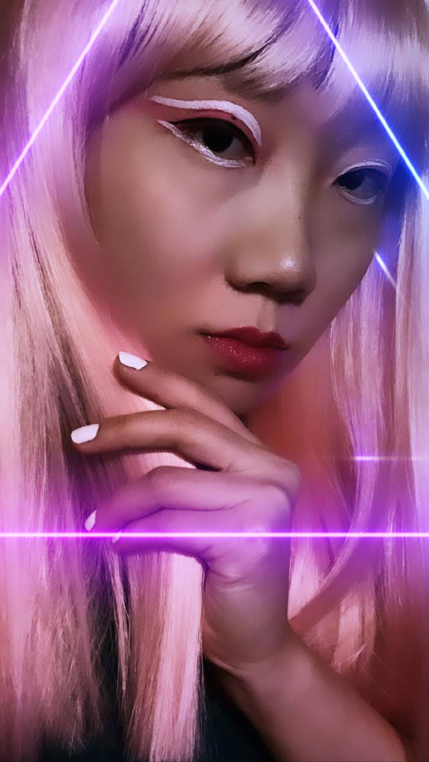 Person with pink wig and neon makeup, posed in front of glowing triangle lines, hand near face, futuristic aesthetic.