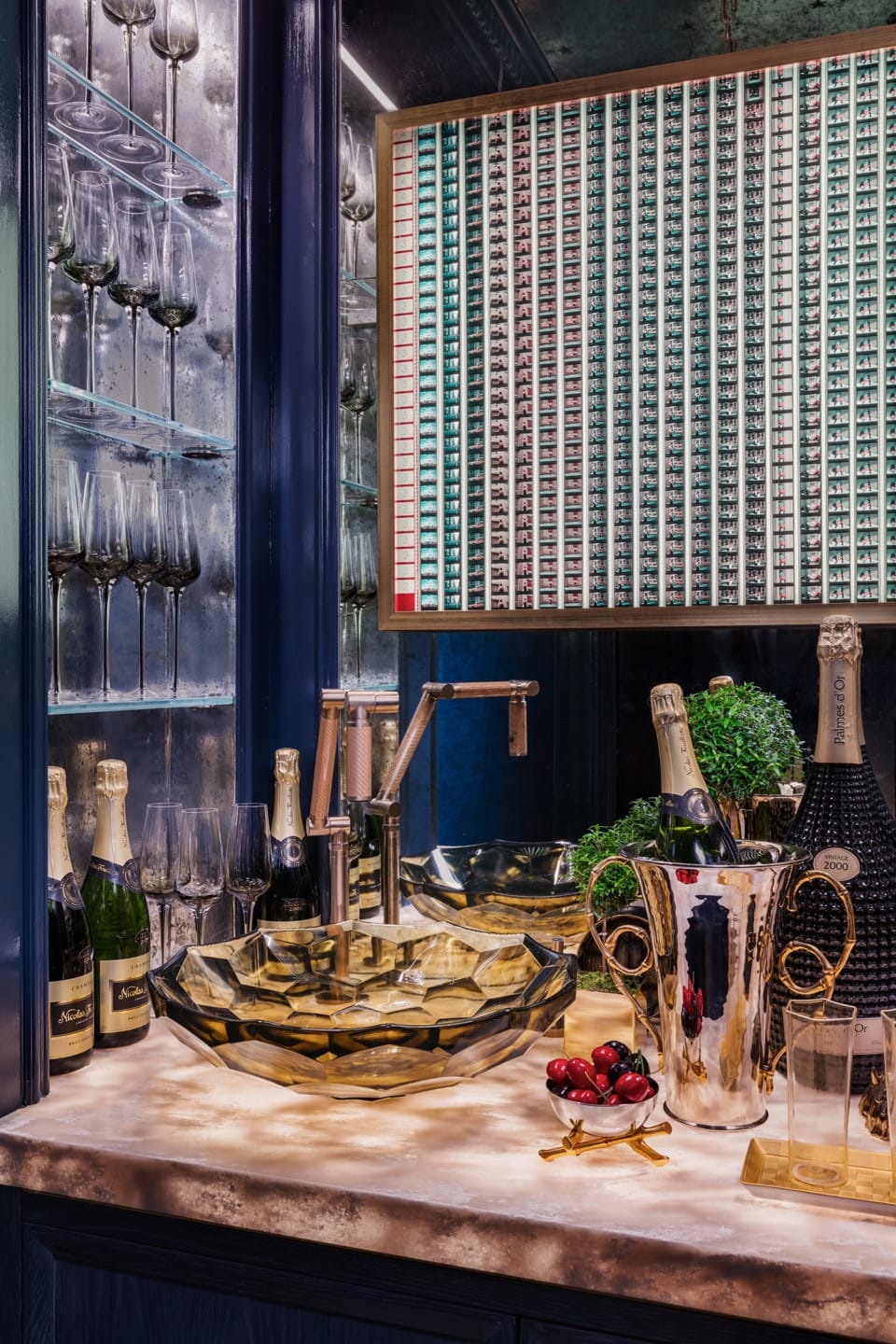 Luxurious home bar with champagne bottles, glassware on shelves, and decorative fruit bowl on a marble countertop.