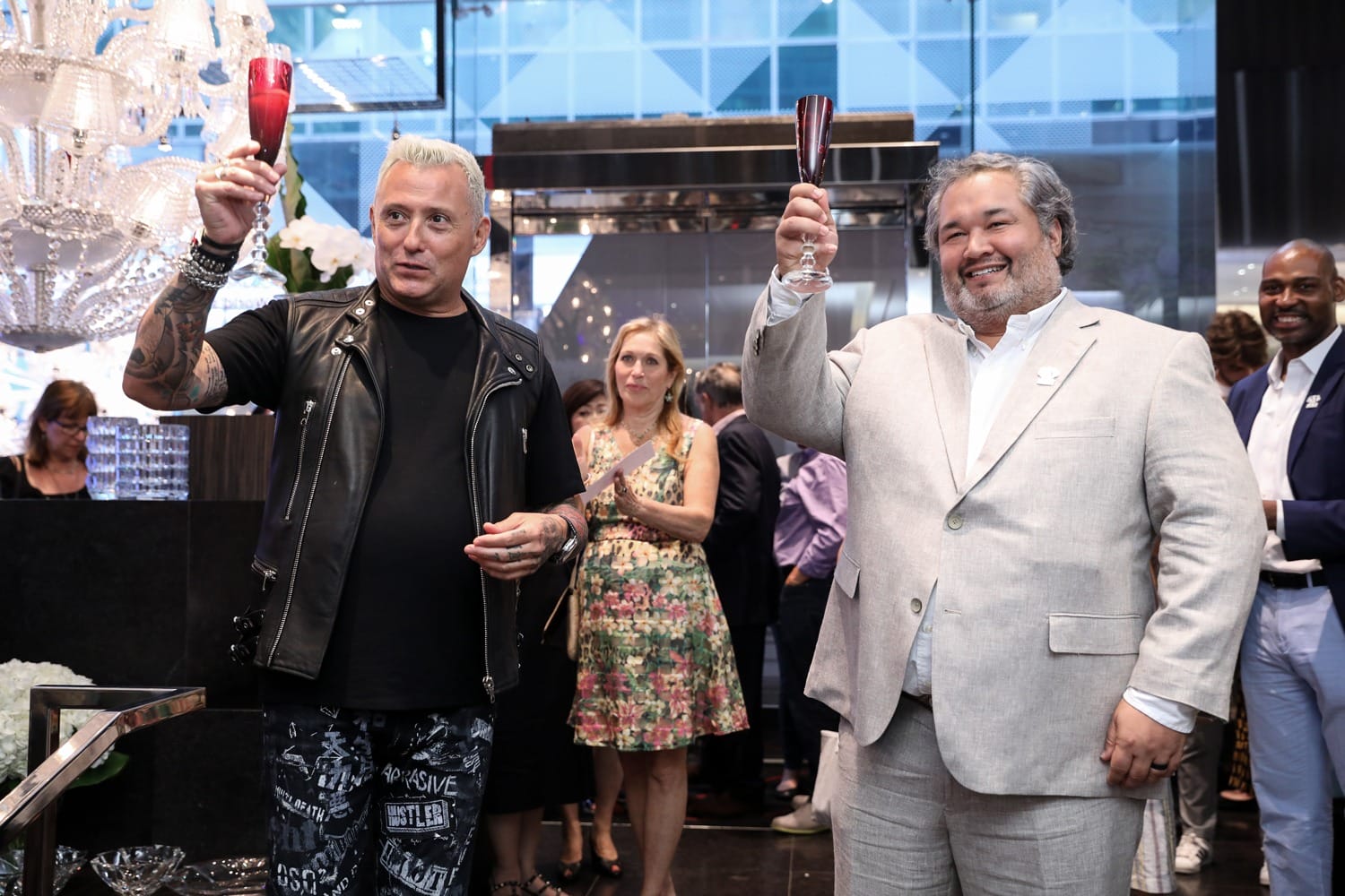 Two men raising glasses in a celebratory toast at a formal event, with people in the background.
