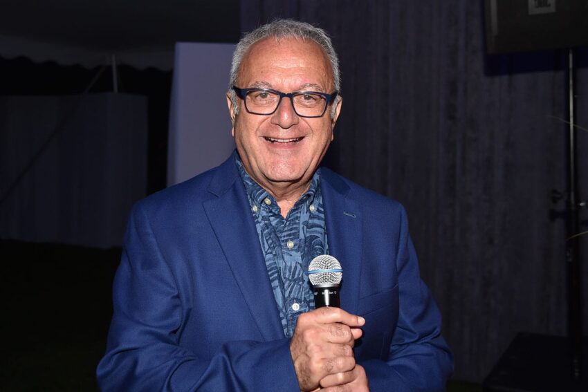 Man in a blue blazer holding a microphone and smiling at an event.