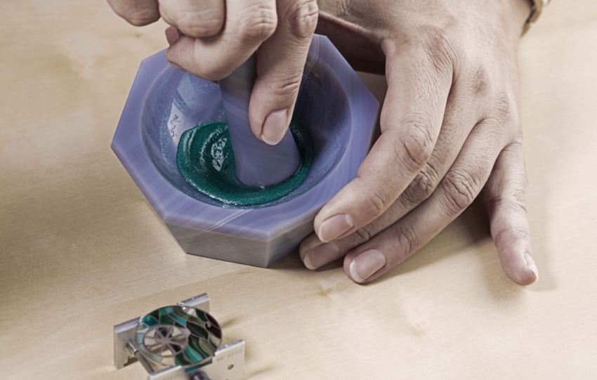 Person grinding green pigment in a mortar with a pestle on a wooden table.