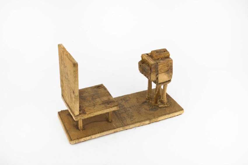 Handcrafted miniature wood sculpture of a chair facing a camera on a white background.