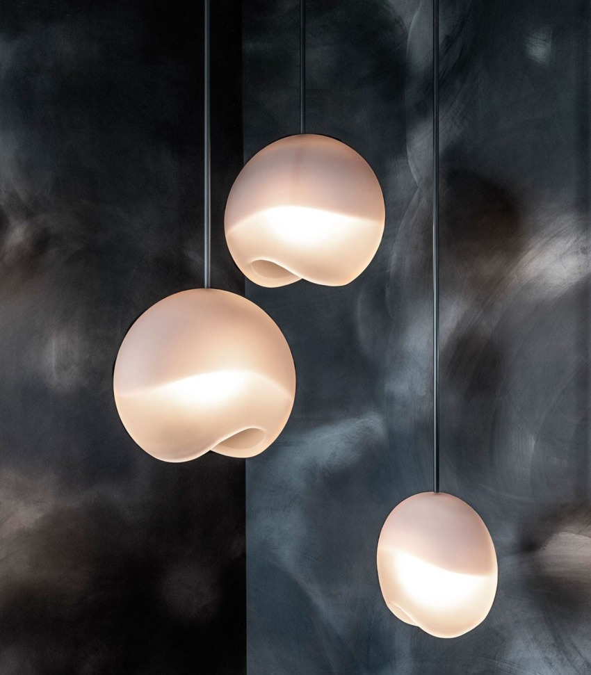 Three modern spherical pendant lights with a smooth, matte finish hanging in front of a textured dark background.