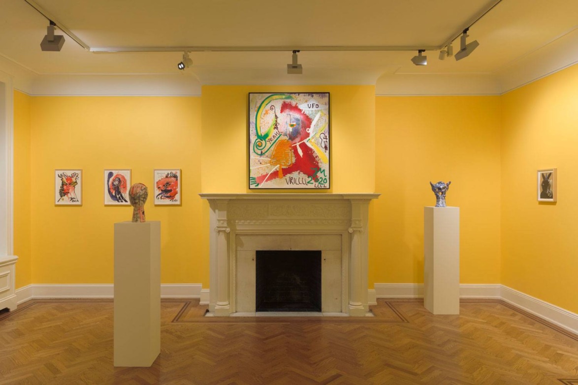 Art gallery with vibrant yellow walls, abstract paintings, and sculptures on white pedestals around a central fireplace.