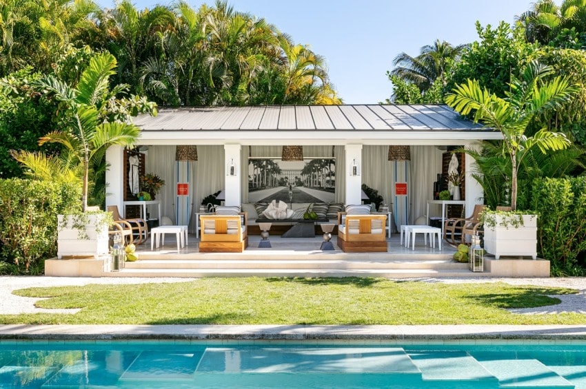 Modern poolside cabana surrounded by lush greenery with comfortable seating and a small bar area.