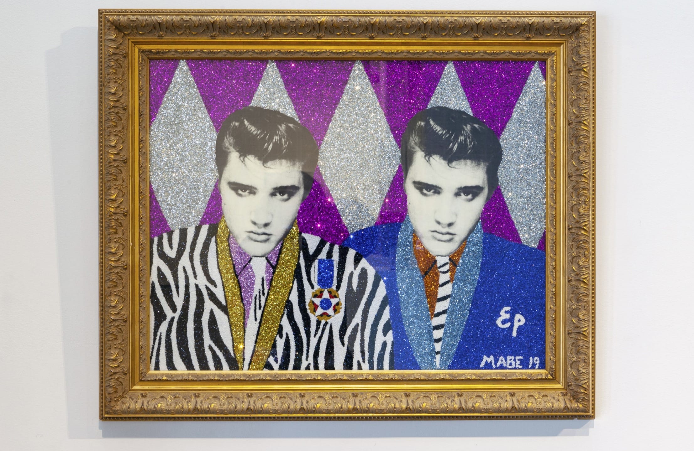 Artwork of two figures in patterned suits with geometric background in a gold frame.