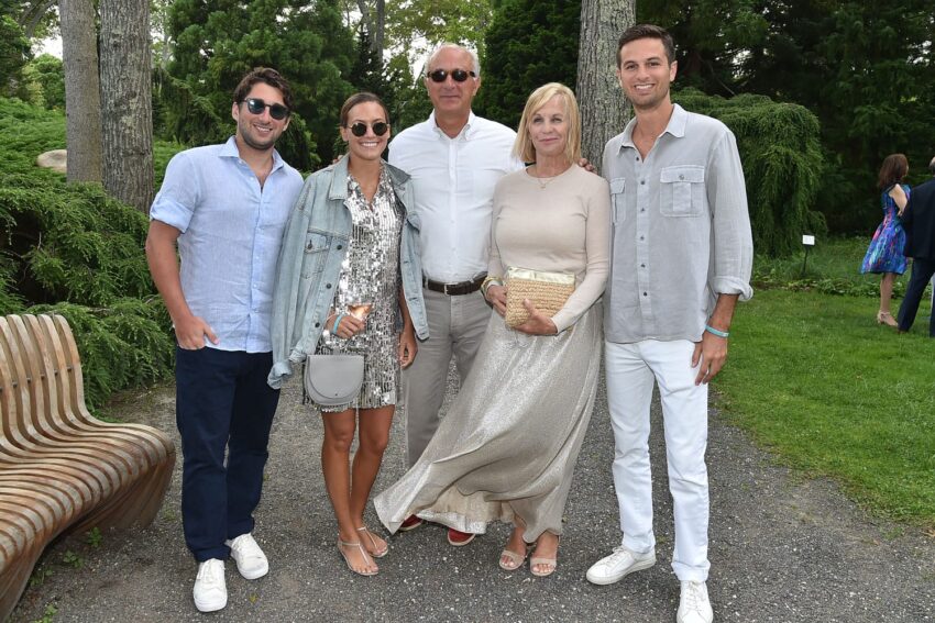 Group of five people posing outdoors in a garden setting, all dressed in light, casual clothing.