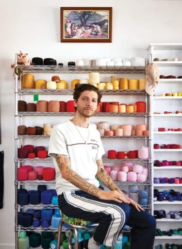 Person sitting in front of shelves filled with colorful yarn balls in a craft room.