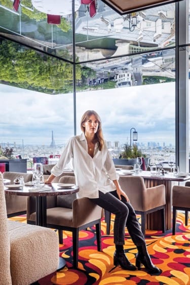 Woman sitting in modern, colorful restaurant with Paris skyline view and unique mirrored ceiling.